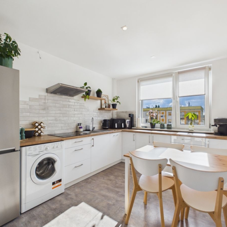 Bright modern kitchen with white cabinets, wooden countertops, and a stainless fridge; a washing machine is tucked under the counter near the left wall.