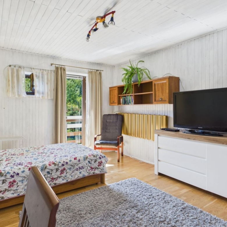 Bright bedroom with a floral quilted bed, white/wood furniture, and a gray armchair by a windowed door to a balcony.