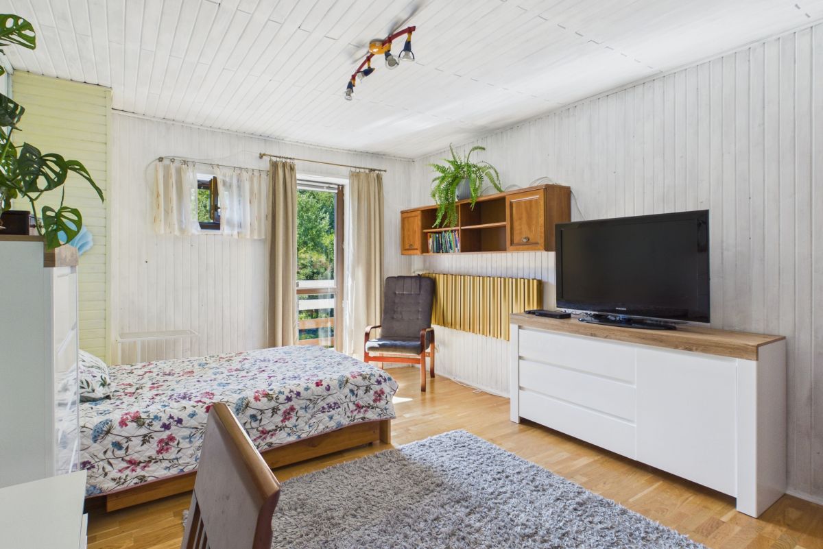 Bright bedroom with a floral quilted bed, white/wood furniture, and a gray armchair by a windowed door to a balcony.