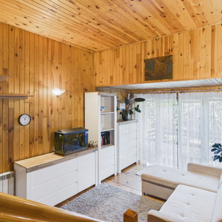 Cozy living room with wooden panel walls, white cabinets, and a beige sofa facing large glass doors with sheer curtains.