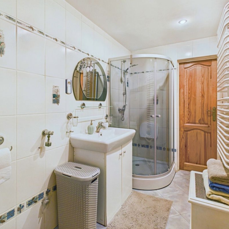 Bathroom with curved corner shower, white sink, round mirror, towel radiator, wooden door, and wicker laundry basket.