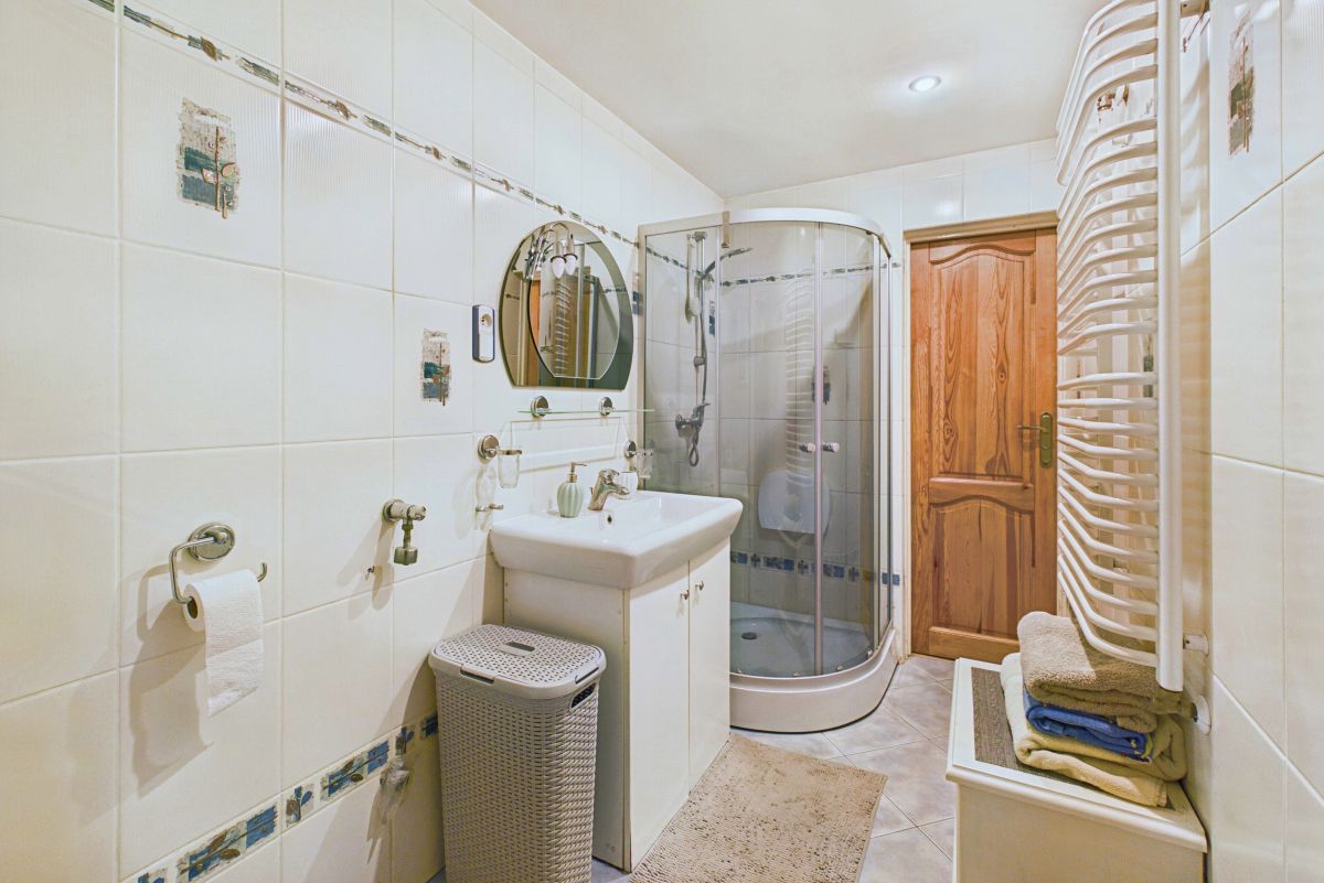 Bathroom with curved corner shower, white sink, round mirror, towel radiator, wooden door, and wicker laundry basket.