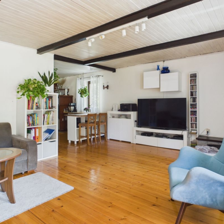 Bright open-plan living room with wooden floors, gray sofa, blue lounge chair, TV stand, and white cabinets.