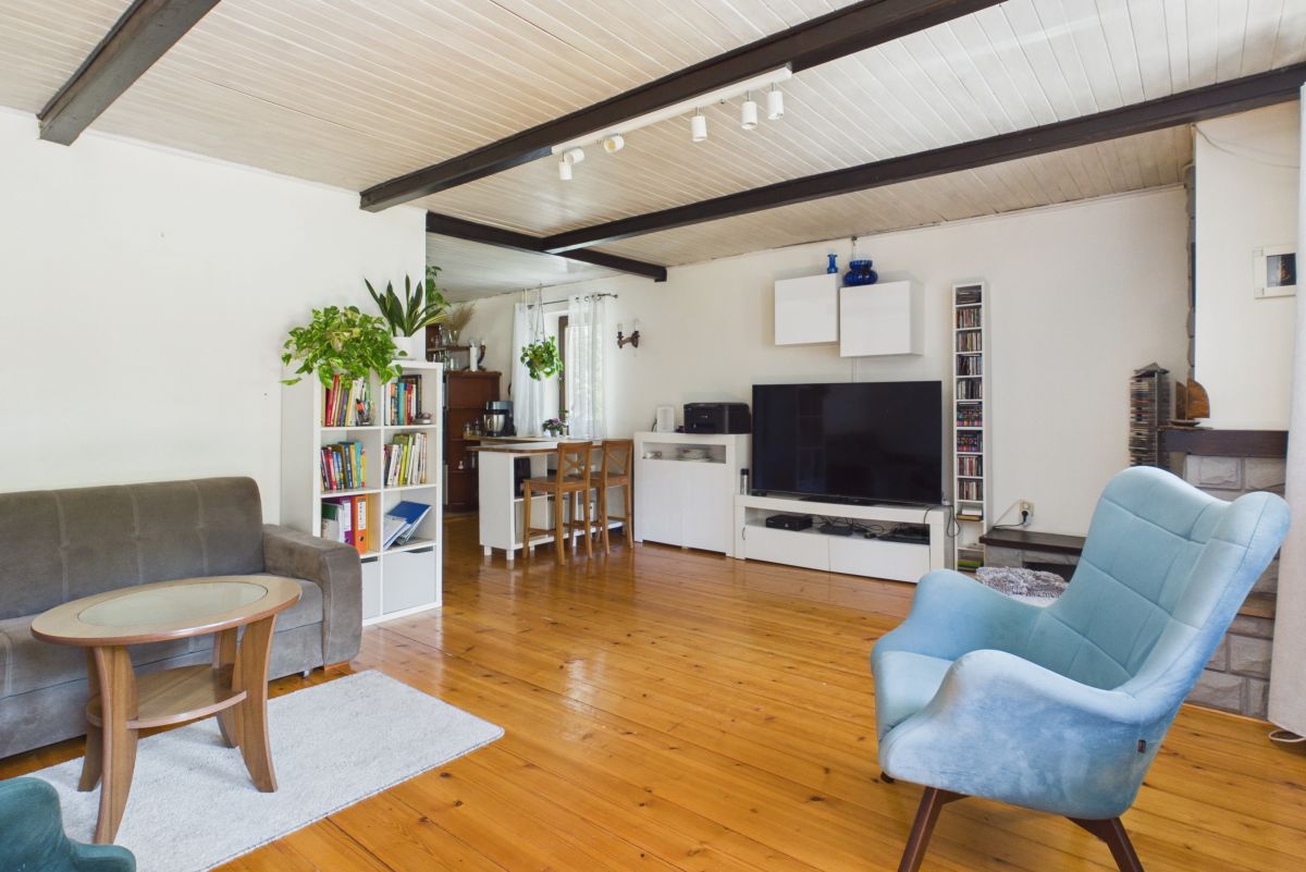 Bright open-plan living room with wooden floors, gray sofa, blue lounge chair, TV stand, and white cabinets.