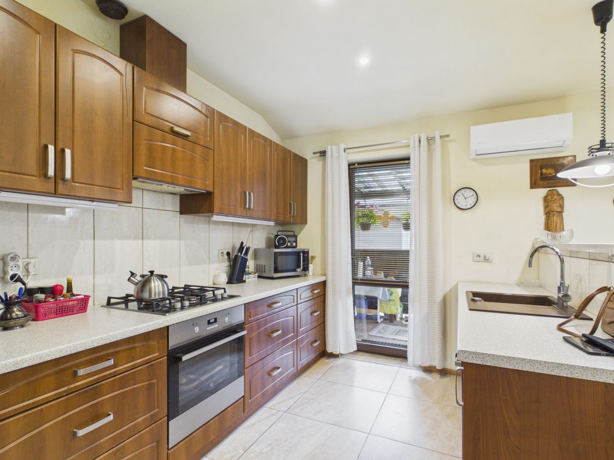 Kitchen with wooden cabinets, gas stove, oven, and kettle on a light counter; window with blinds and curtains at the back.