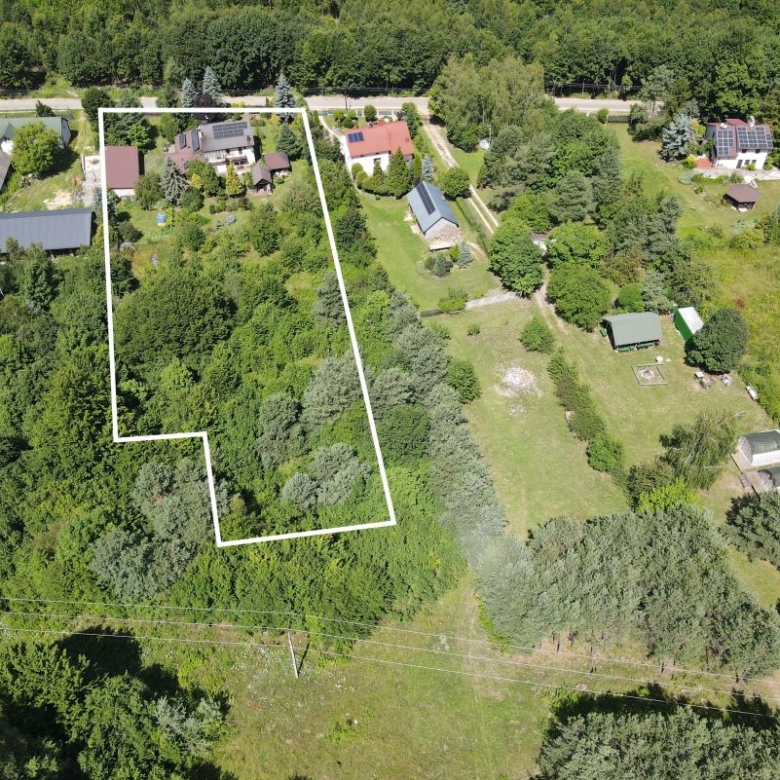 Aerial view of a residential property outlined in white, showing a wooded lot with neighboring homes nearby.