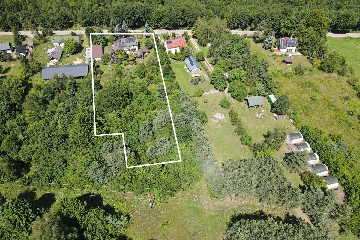 Aerial view of a residential property outlined in white, showing a wooded lot with neighboring homes nearby.