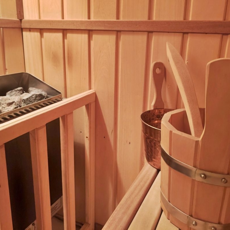 Sauna room with a stone heater, a wooden bucket, and a ladle on a bench inside wooden walls.