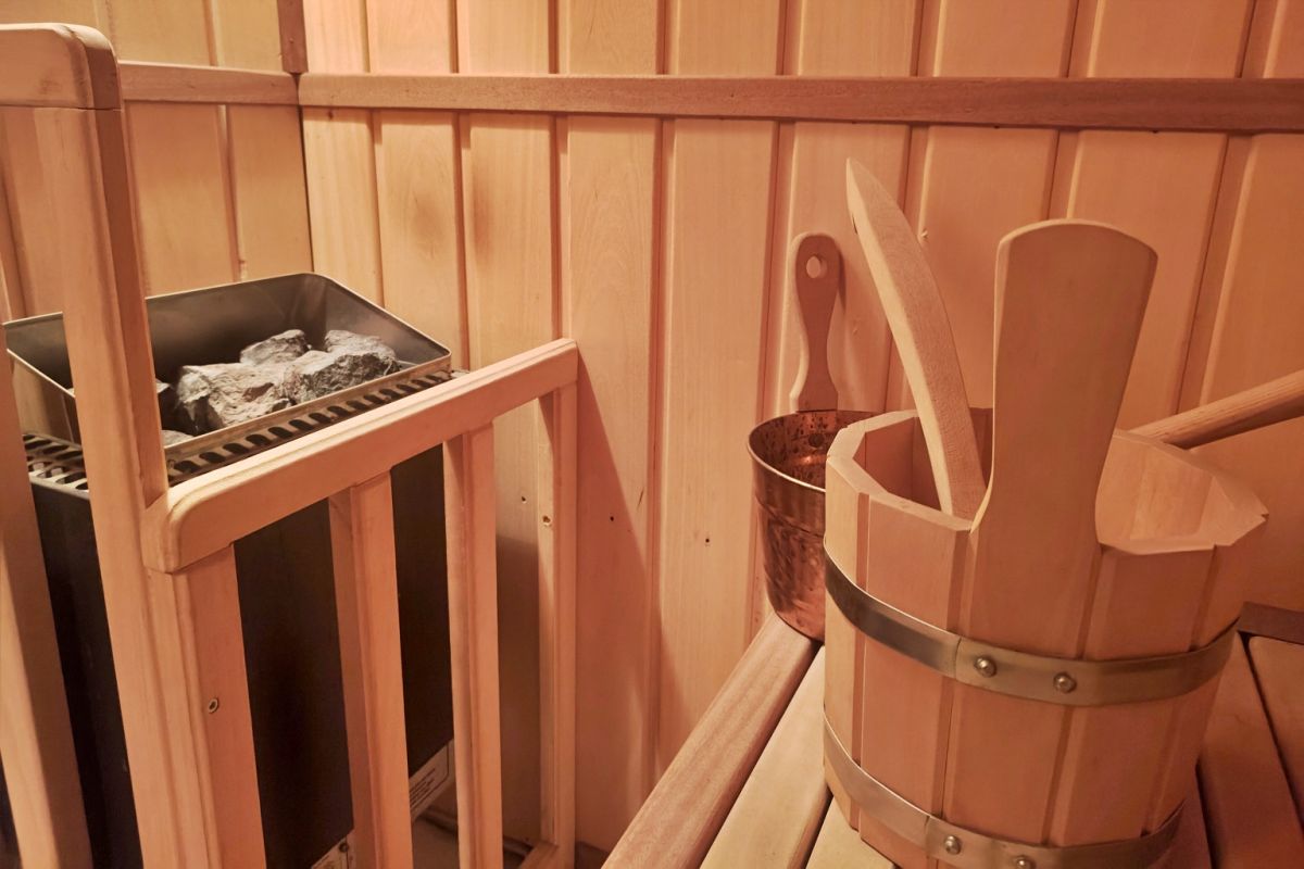 Sauna room with a stone heater, a wooden bucket, and a ladle on a bench inside wooden walls.