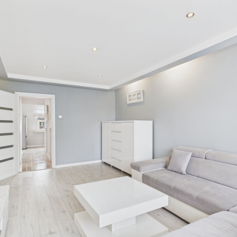 Bright, minimalist living room with light gray walls, white coffee table and sofa, and a white dresser against the wall.