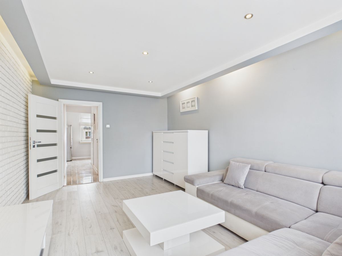 Bright, minimalist living room with light gray walls, white coffee table and sofa, and a white dresser against the wall.