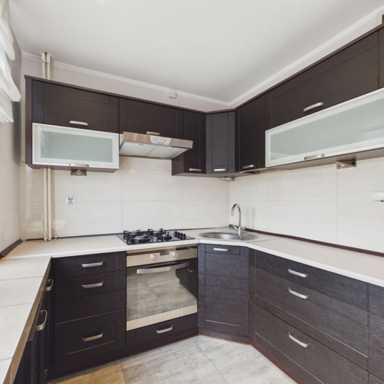 L-shaped kitchen with dark cabinets, white countertops, gas cooktop, and stainless oven under a frosted glass cabinet.