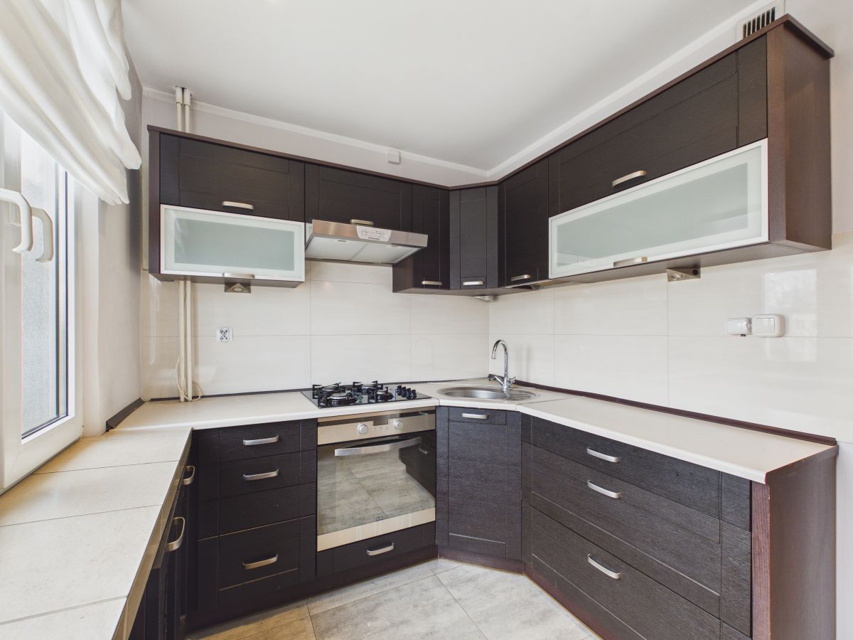 L-shaped kitchen with dark cabinets, white countertops, gas cooktop, and stainless oven under a frosted glass cabinet.