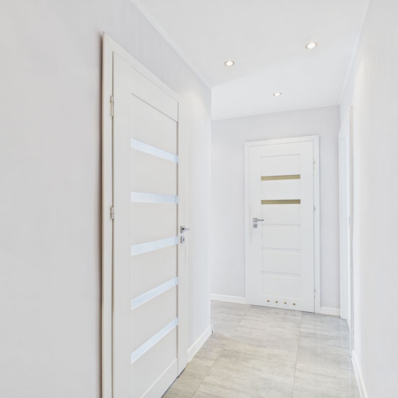 Bright white hallway with two modern white doors featuring horizontal frosted glass panels and recessed ceiling lights on a light tiled floor
