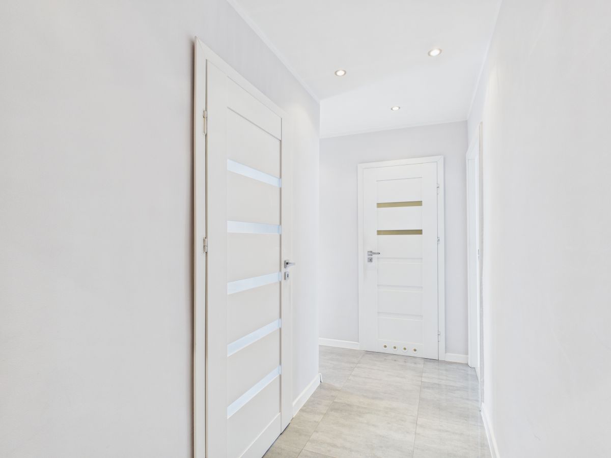Bright white hallway with two modern white doors featuring horizontal frosted glass panels and recessed ceiling lights on a light tiled floor