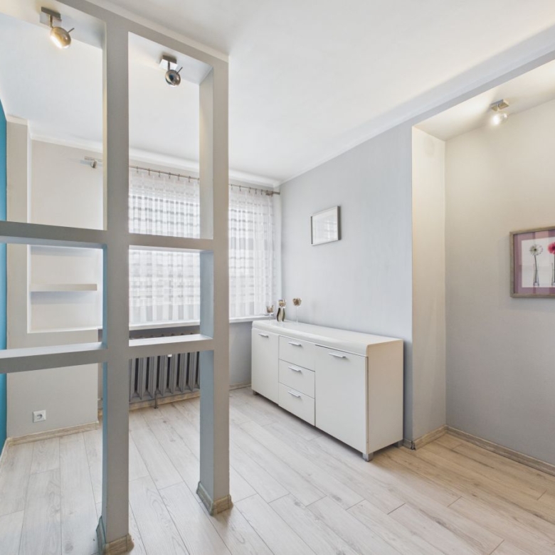 Bright modern room with a white sideboard, gray walls, and a decorative partition of square-framed panels near a window with sheer curtains.