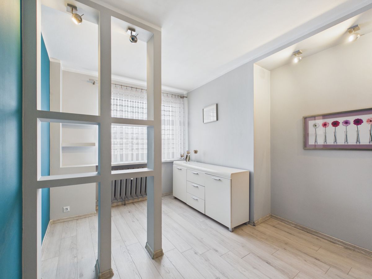 Bright modern room with a white sideboard, gray walls, and a decorative partition of square-framed panels near a window with sheer curtains.