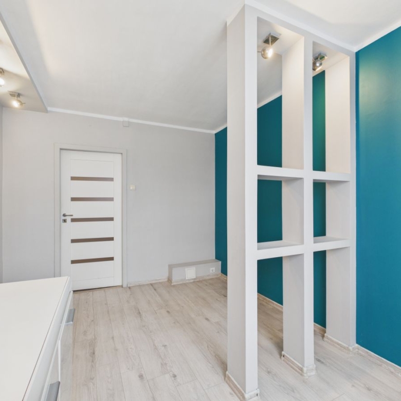 Modern hallway with teal accent wall and white partition featuring square openings behind which another room is visible.