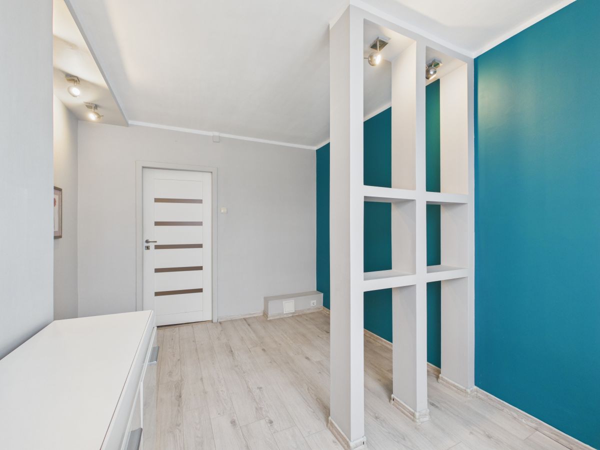 Modern hallway with teal accent wall and white partition featuring square openings behind which another room is visible.