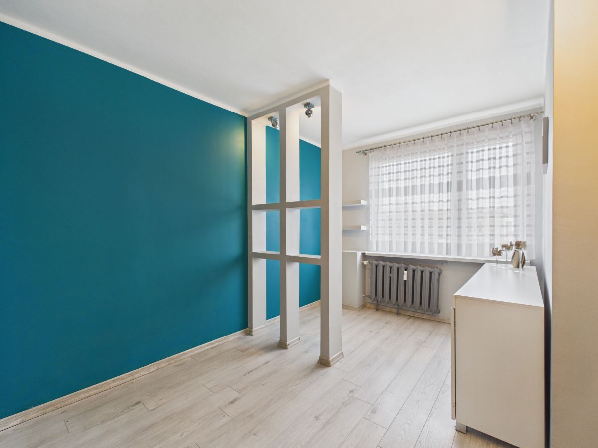 Modern minimalist room with a teal accent wall, a white grid divider, and a white dresser by a window with sheer curtains.