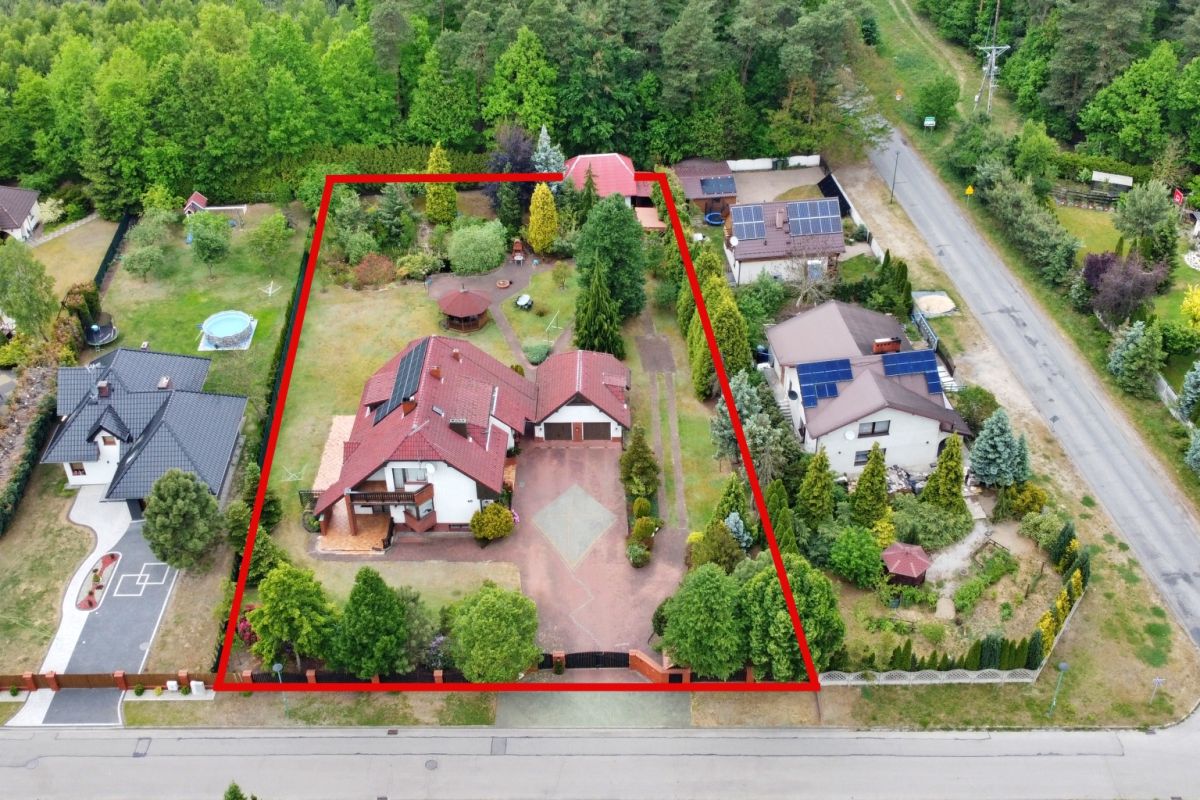 Aerial view of a residential property with a red boundary outline enclosing a two-story house, driveway, garden, and trees.