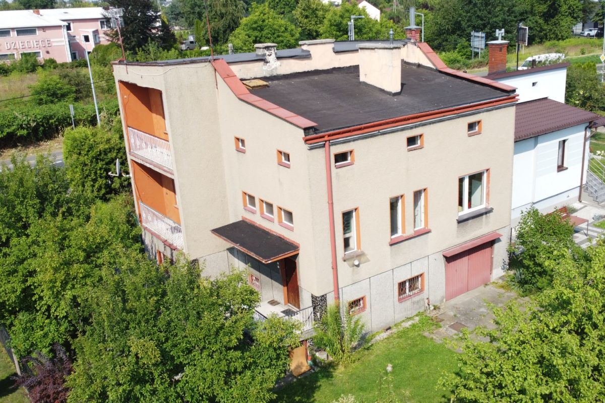 Aerial view of a beige, three-story apartment building with orange balconies, red gutters, and a flat black roof, surrounded by trees and greenery.