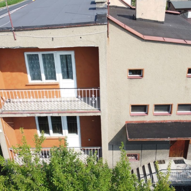 Aerial view of a two-story beige stucco building with orange inner walls, white balcony railings, and a white door on the upper balcony.
