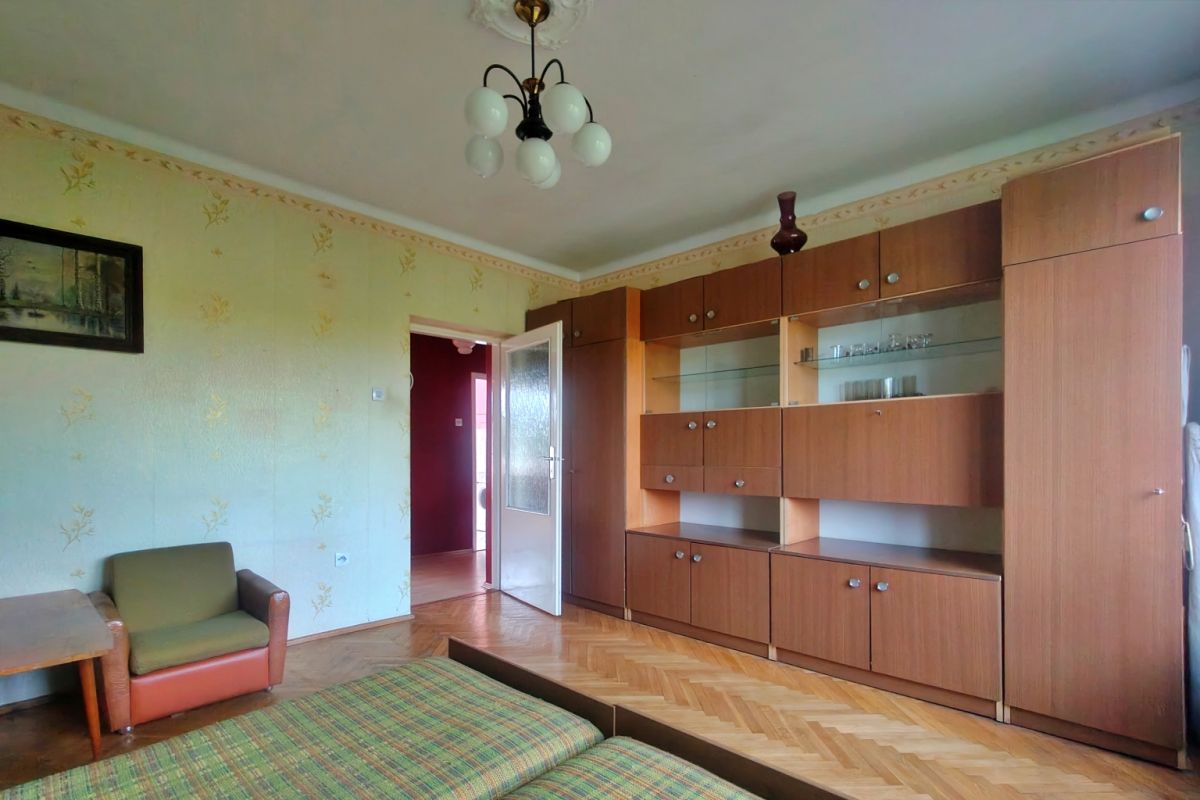 Living room with a large wooden wall cabinet, green plaid sofa, and an orange-brown armchair on a parquet floor.