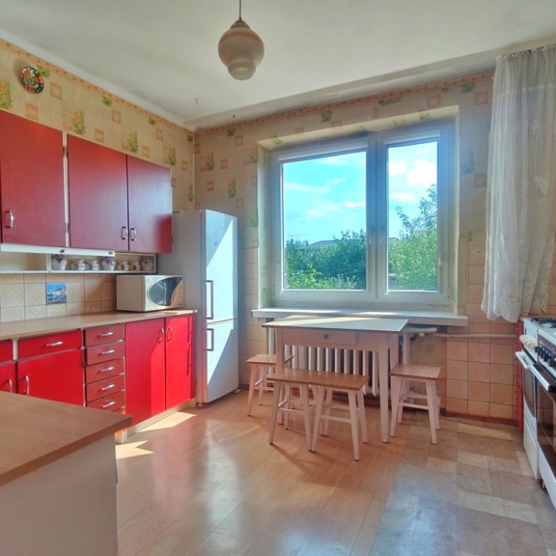 Retro kitchen with red cabinets, tiled walls, and a white dining table with stools by a large window with a green view.