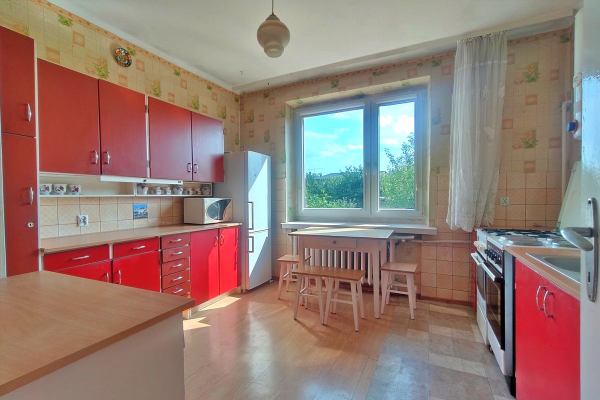 Retro kitchen with red cabinets, tiled walls, and a white dining table with stools by a large window with a green view.
