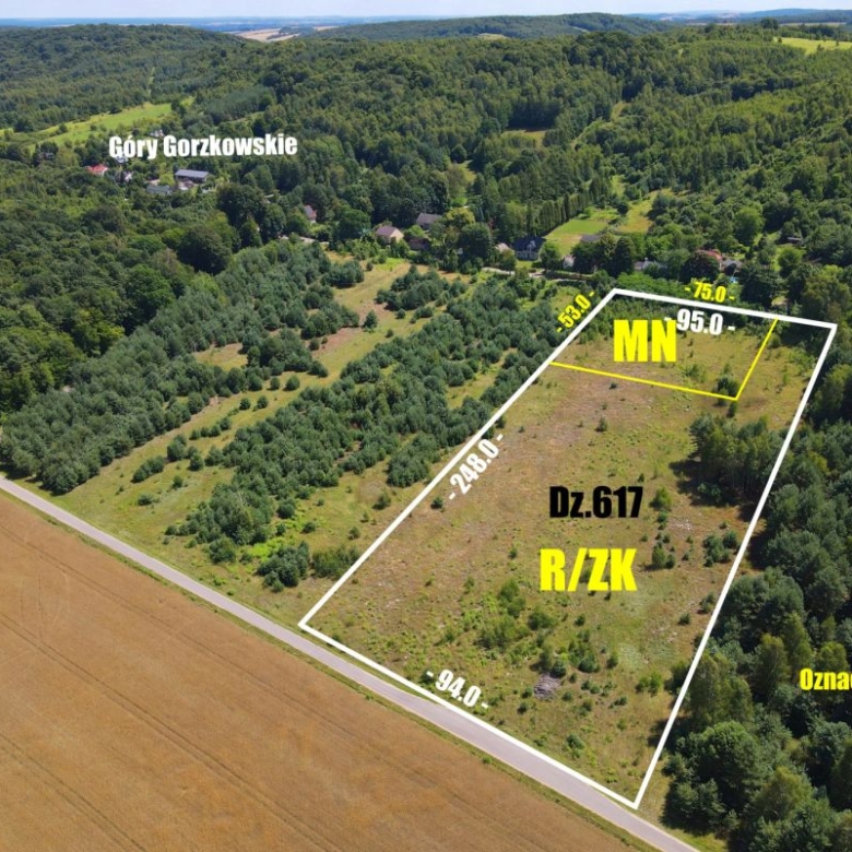 Aerial view of a rectangular land parcel outlined in white with edge measurements, labeled MN for residential zoning and Dz.617 R/ZK, surrounded by forest and fields.