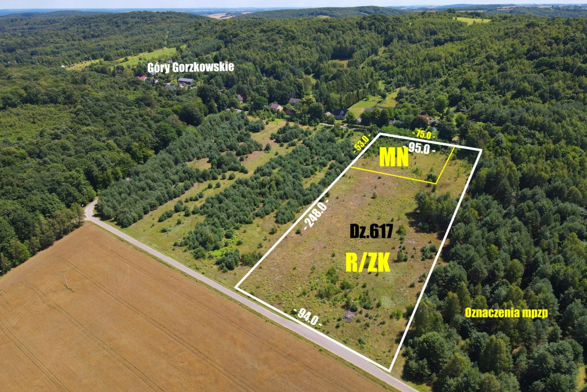 Aerial view of a rectangular land parcel outlined in white with edge measurements, labeled MN for residential zoning and Dz.617 R/ZK, surrounded by forest and fields.