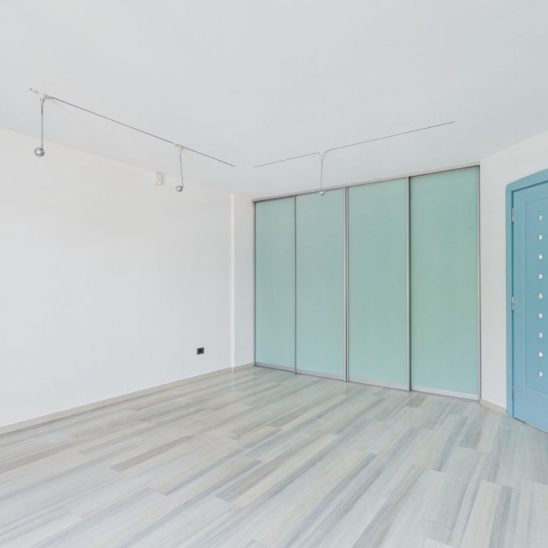 Empty white room with gray wood floor, frosted glass sliding closet doors, and a blue entry door. Track lighting lines the ceiling.