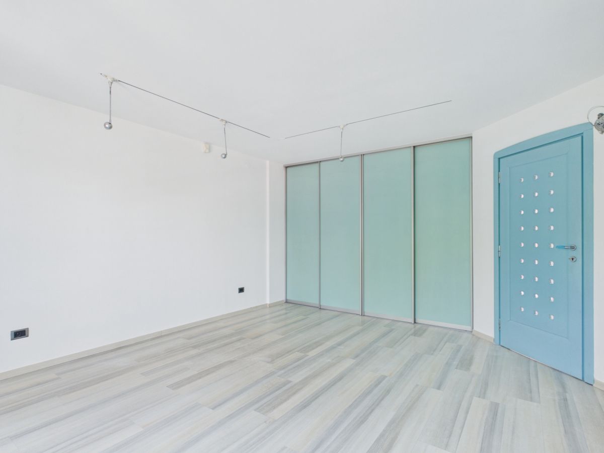Empty white room with gray wood floor, frosted glass sliding closet doors, and a blue entry door. Track lighting lines the ceiling.