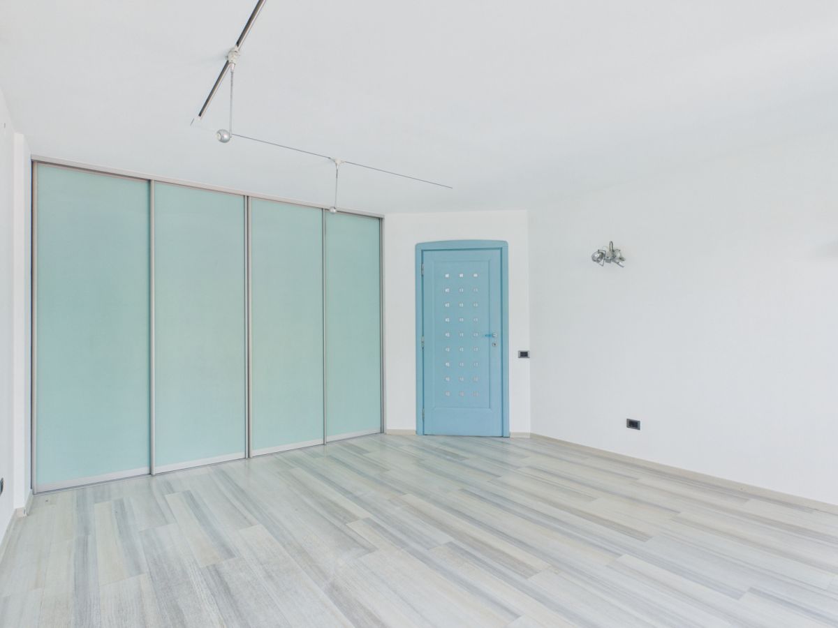 Bright minimalist room with light wood floor, pale frosted glass sliding panels on the left and a blue door with square cutouts.
