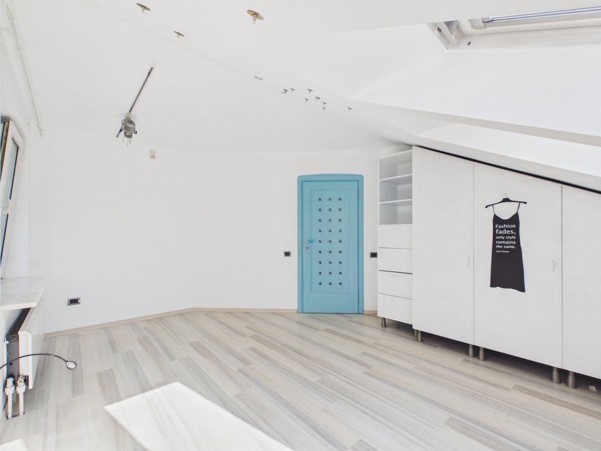 Bright white attic studio with light wood floor, blue door, white cabinets, and a black dress poster on the wardrobe.