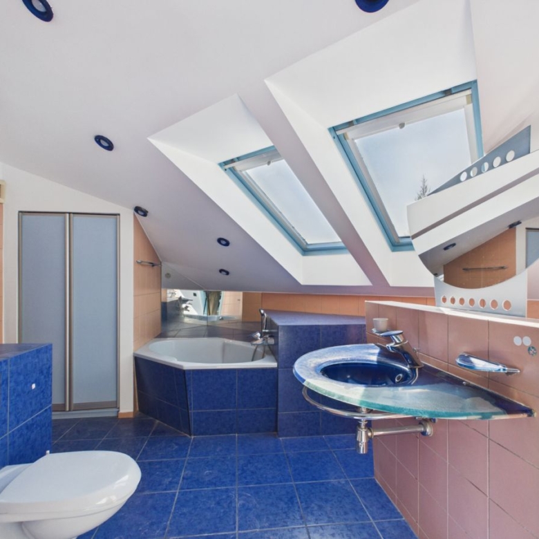 Bright modern bathroom with blue tiled floor and walls, a corner bathtub, and a blue glass sink under angled skylights in a white ceiling.
