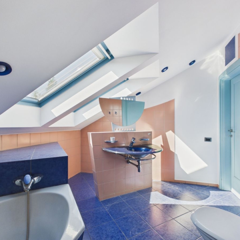 Bright modern bathroom with peach tile walls, blue accents, and a skylight casting geometric light on a pedestal sink area and bathtub.