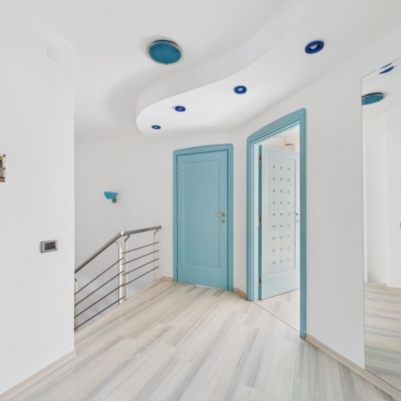 Bright, modern hallway with light wood floors, white walls, and turquoise door frames; curved ceiling with blue recessed lights.