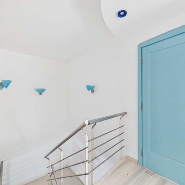 Bright stair landing with white walls, a turquoise door, and blue wall sconces along the stairs,