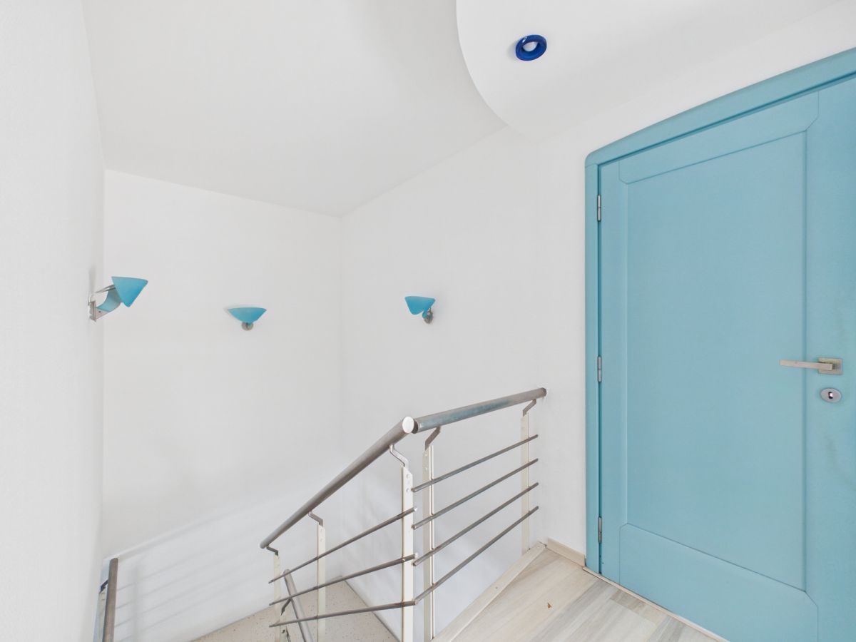 Bright stair landing with white walls, a turquoise door, and blue wall sconces along the stairs,
