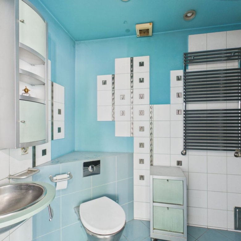 Retro bathroom with turquoise walls, white tile accents, a wall-mounted sink, and a white toilet beside a tall modular cabinet.
