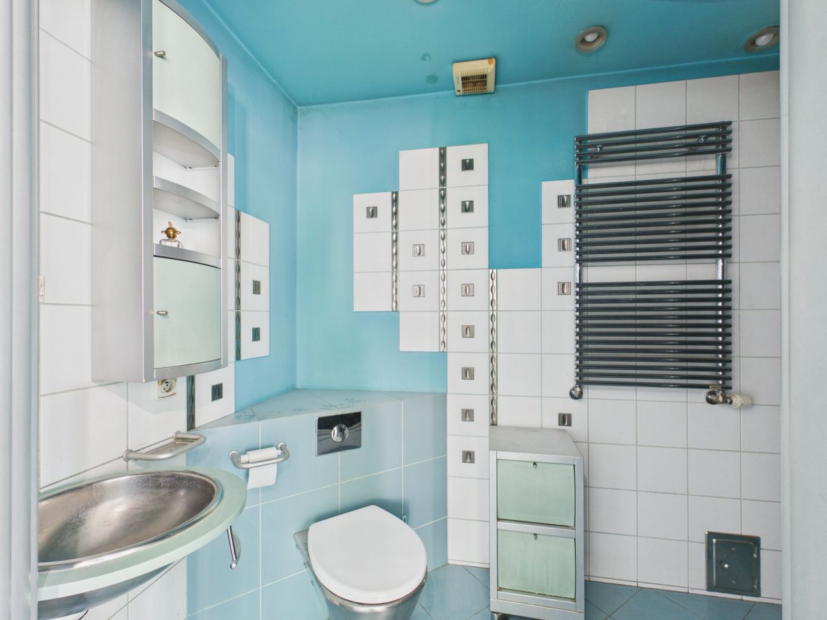 Retro bathroom with turquoise walls, white tile accents, a wall-mounted sink, and a white toilet beside a tall modular cabinet.