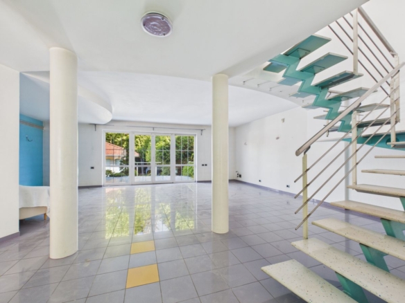 Spacious empty living area with tiled floor, white walls, and a teal metal staircase on the right.
