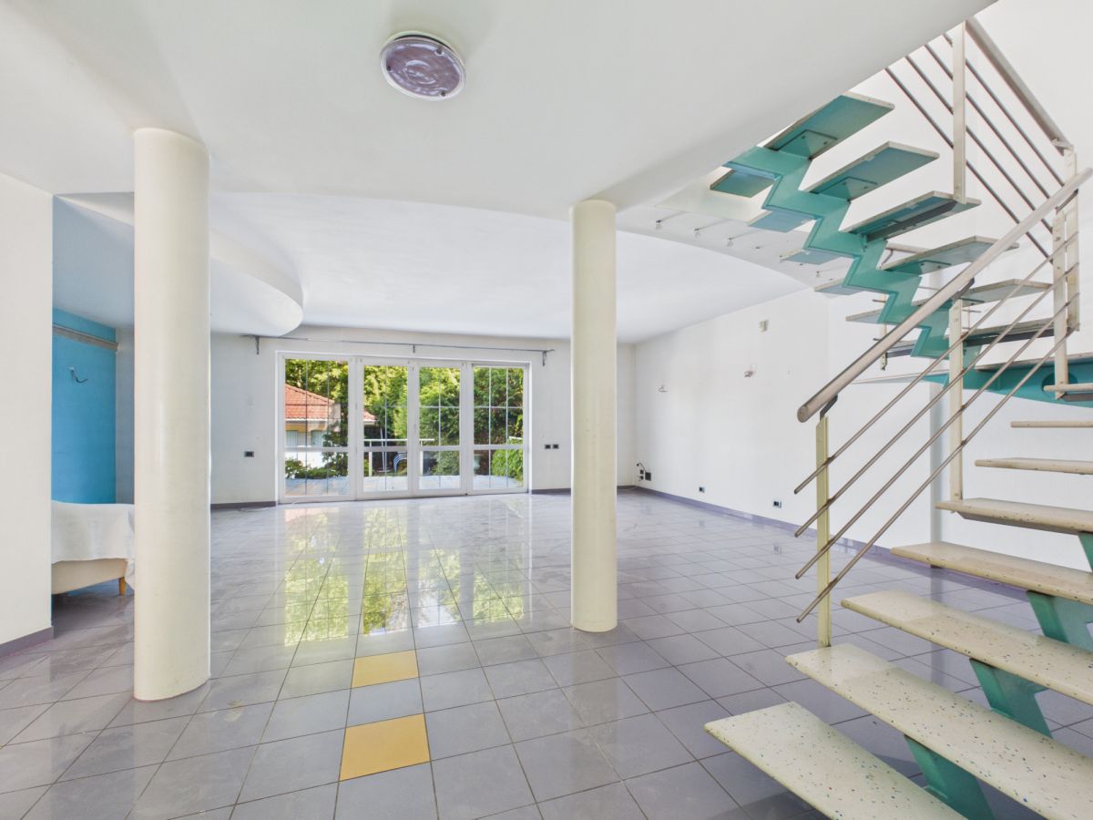Spacious empty living area with tiled floor, white walls, and a teal metal staircase on the right.