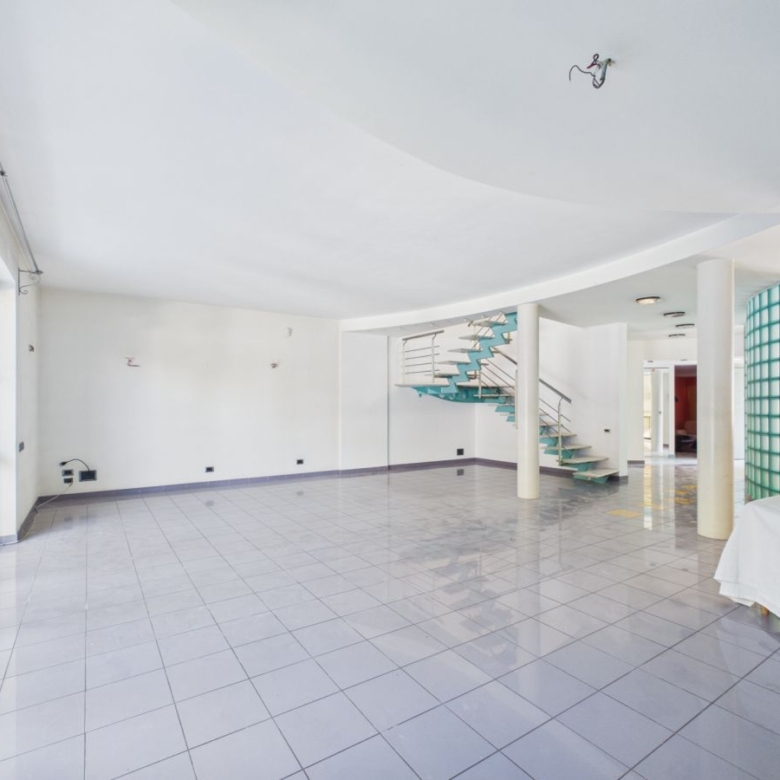 Bright, empty living area with large windows, white walls, and a teal spiral staircase in the center.