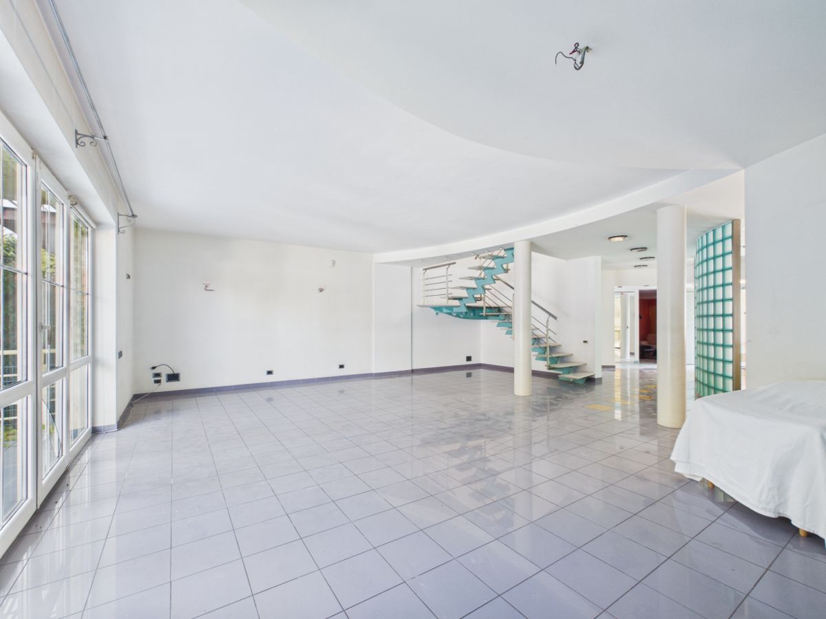 Bright, empty living area with large windows, white walls, and a teal spiral staircase in the center.