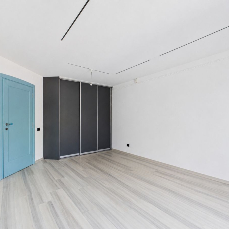Bright empty room with a blue door on the left and a dark wardrobe against the back wall.