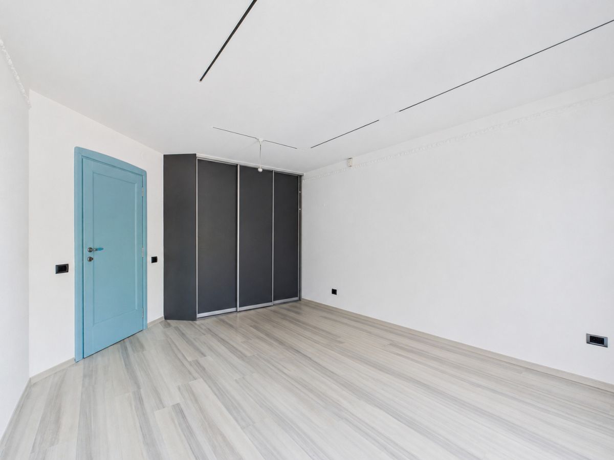 Bright empty room with a blue door on the left and a dark wardrobe against the back wall.