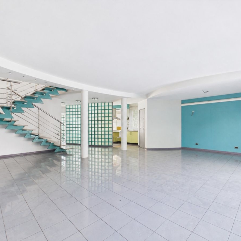 Empty modern interior with a teal zigzag staircase along the left wall, glass block wall, and turquoise accent wall.